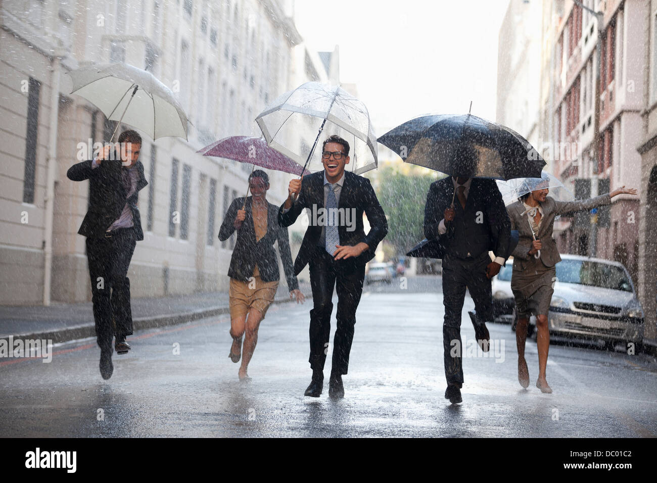 Geschäftsleute mit Sonnenschirmen im verregneten Straße laufen Stockfoto