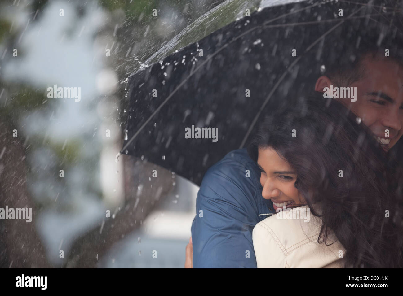 Glückliches Paar umarmt unter Dach im Regen Stockfoto