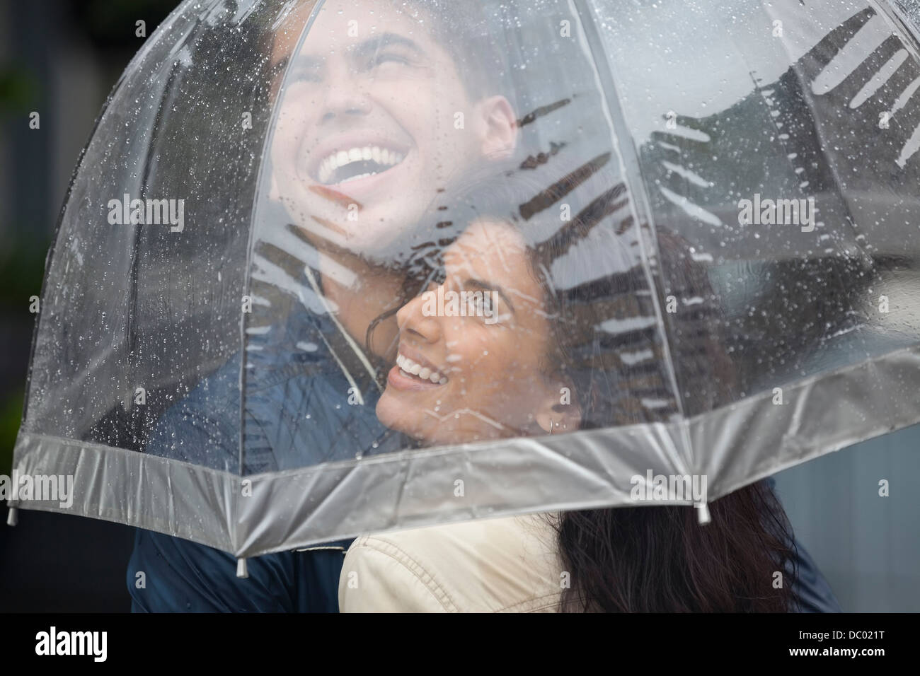 Glückliches Paar unter Dach blickte zu Regen Stockfoto