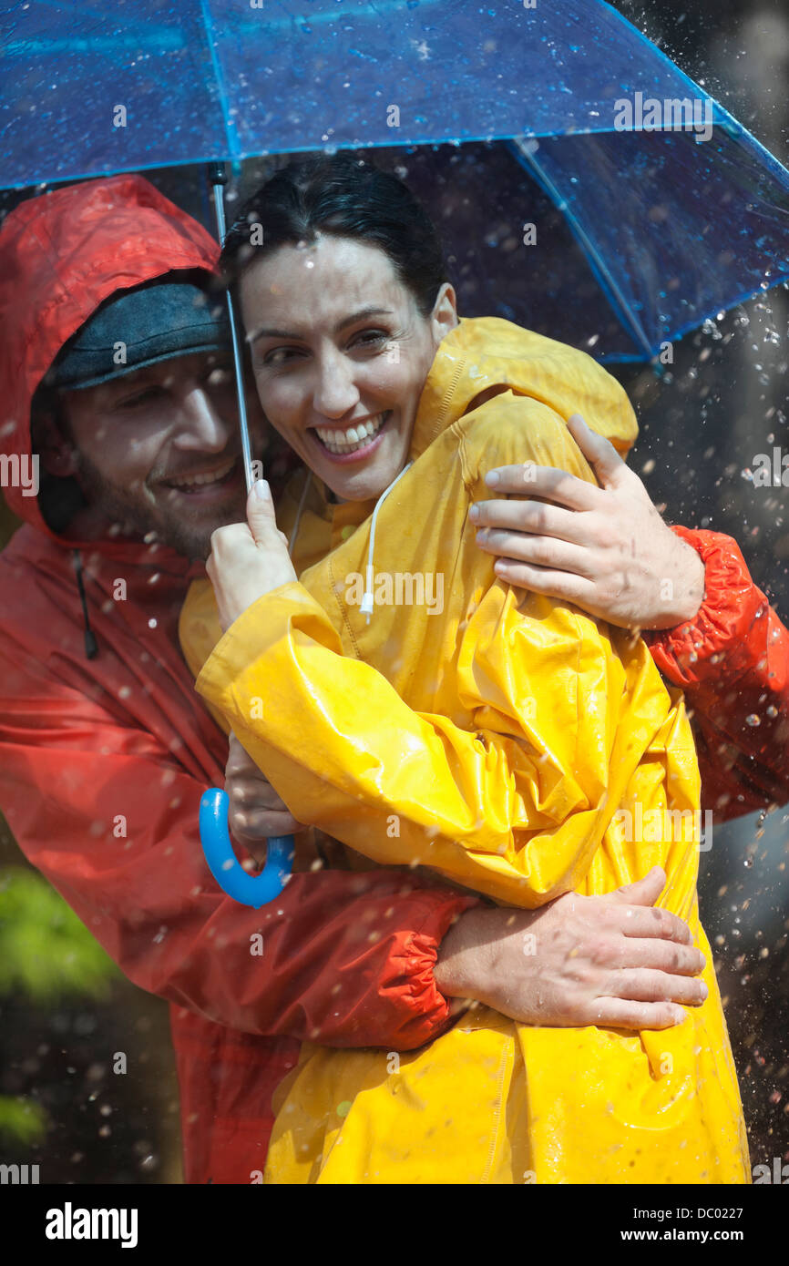 Glückliches Paar umarmt unter Dach im Regen Stockfoto