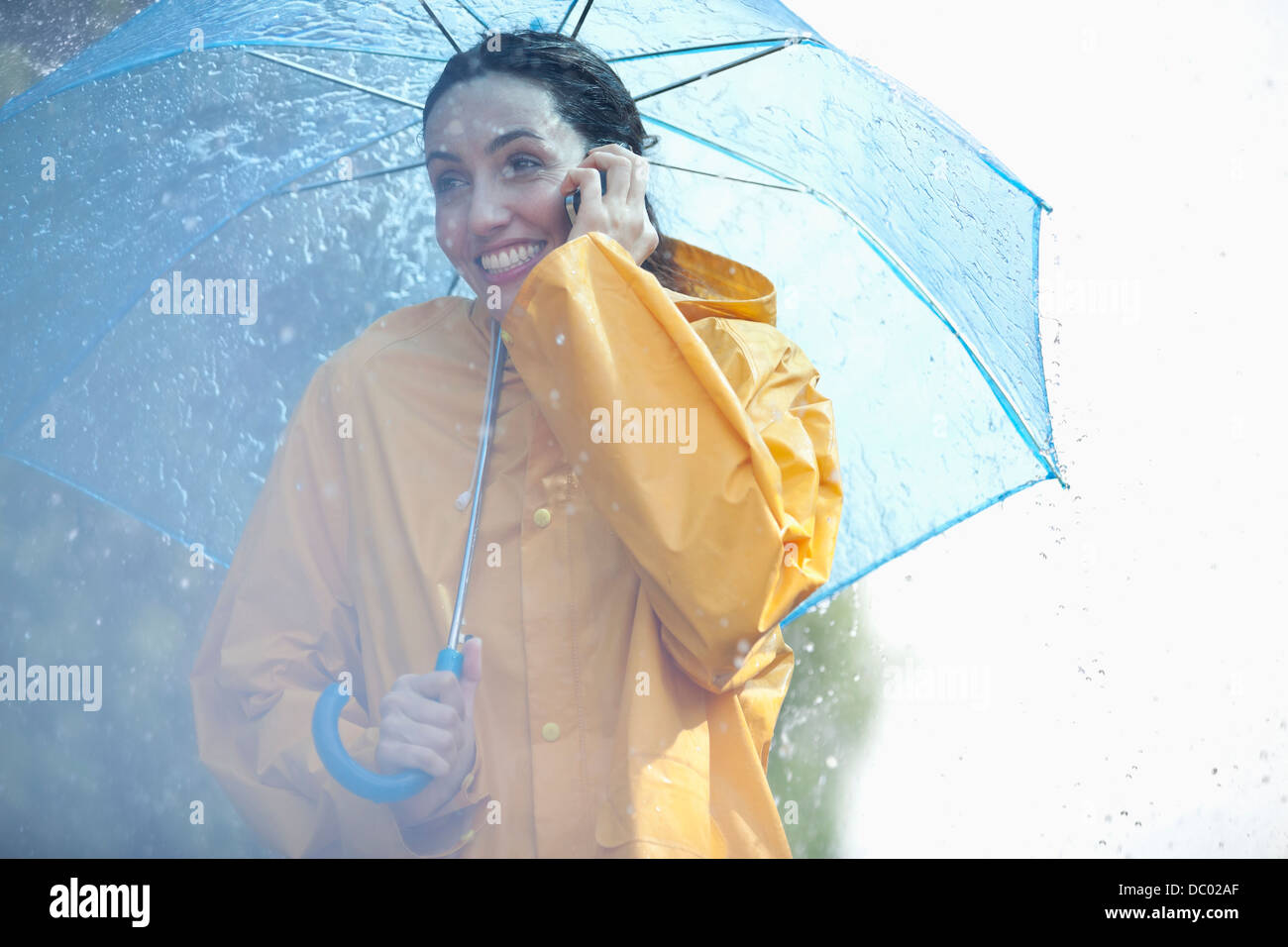 Glückliche Frau am Handy unter Dach im Regen Stockfoto