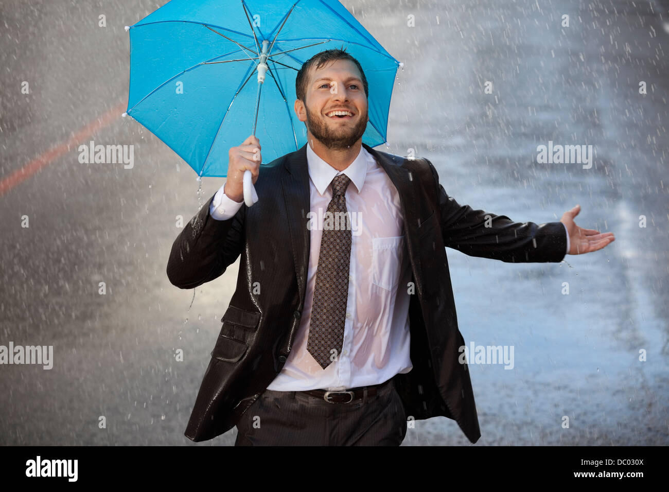 Begeisterte Unternehmer mit kleinen Regenschirm im verregneten Straße Stockfoto