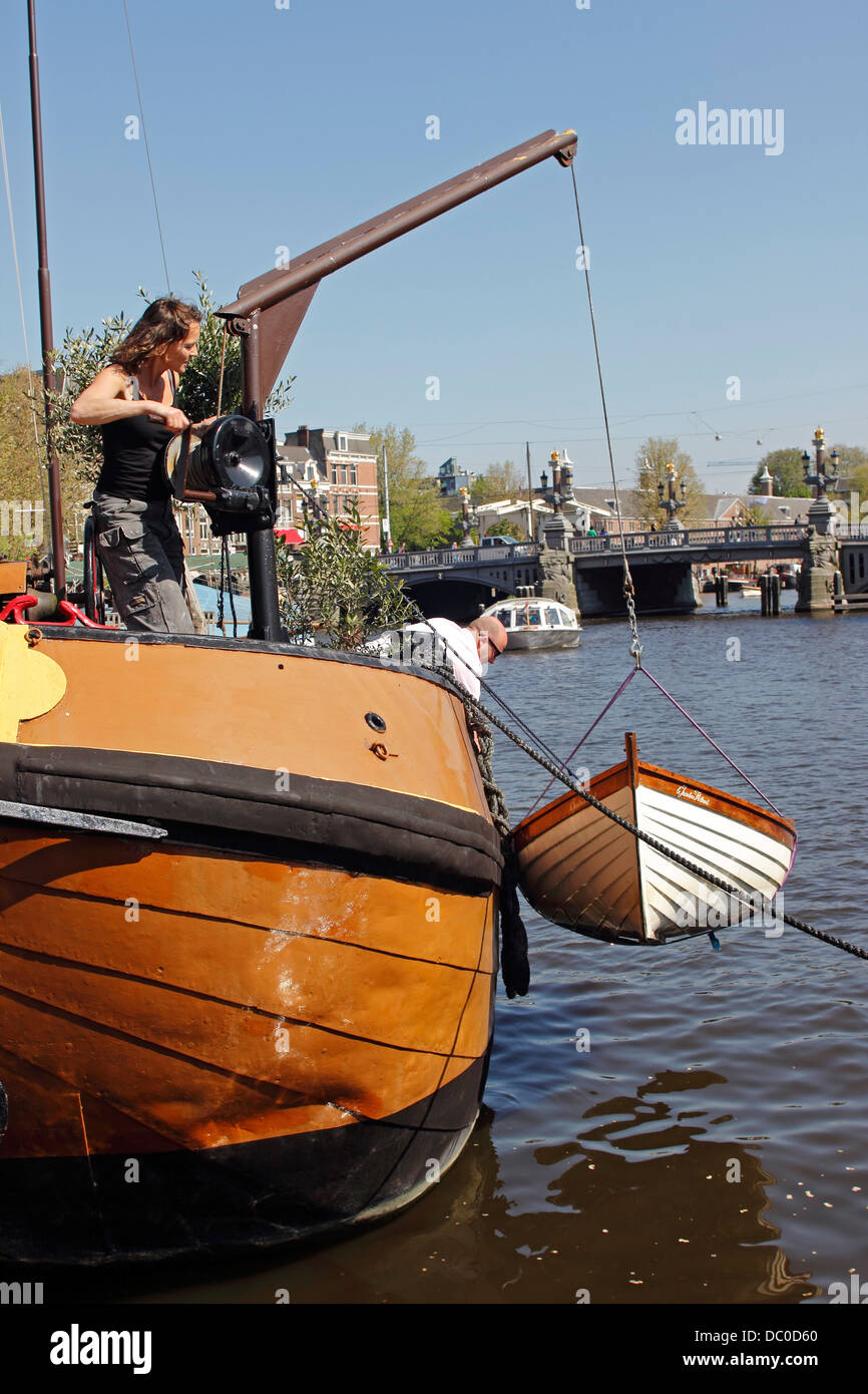 Amsterdam Niederlande Holland Europa Mann und Frau zu senken ein kleines Skiff von Hausboot entlang der Amstel Kanal Stockfoto