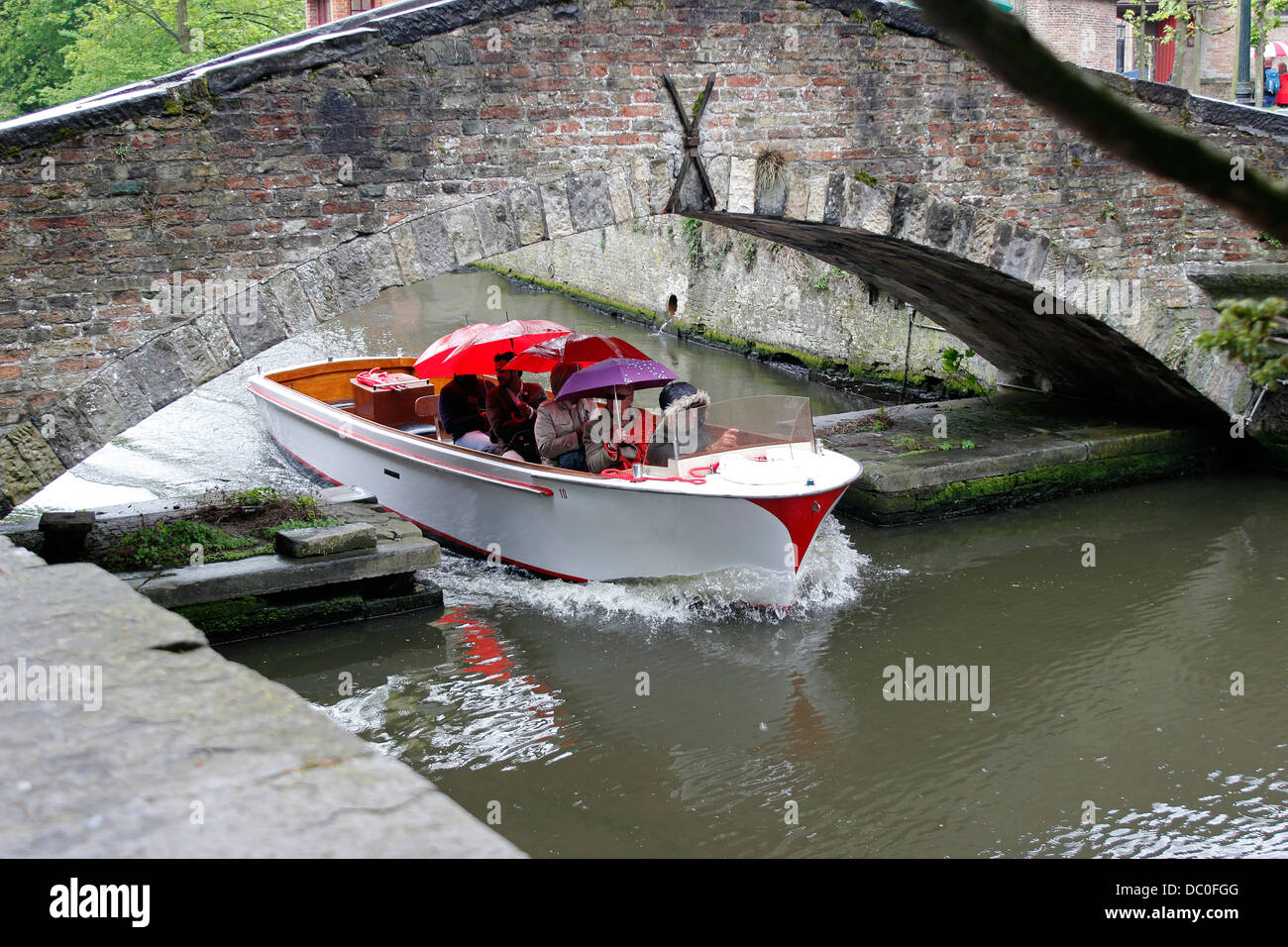 Brügge Belgien Flandern Europa Brugge Touristenboot Tour unter steinerne Brücke im Regen mit Sonnenschirmen Stockfoto