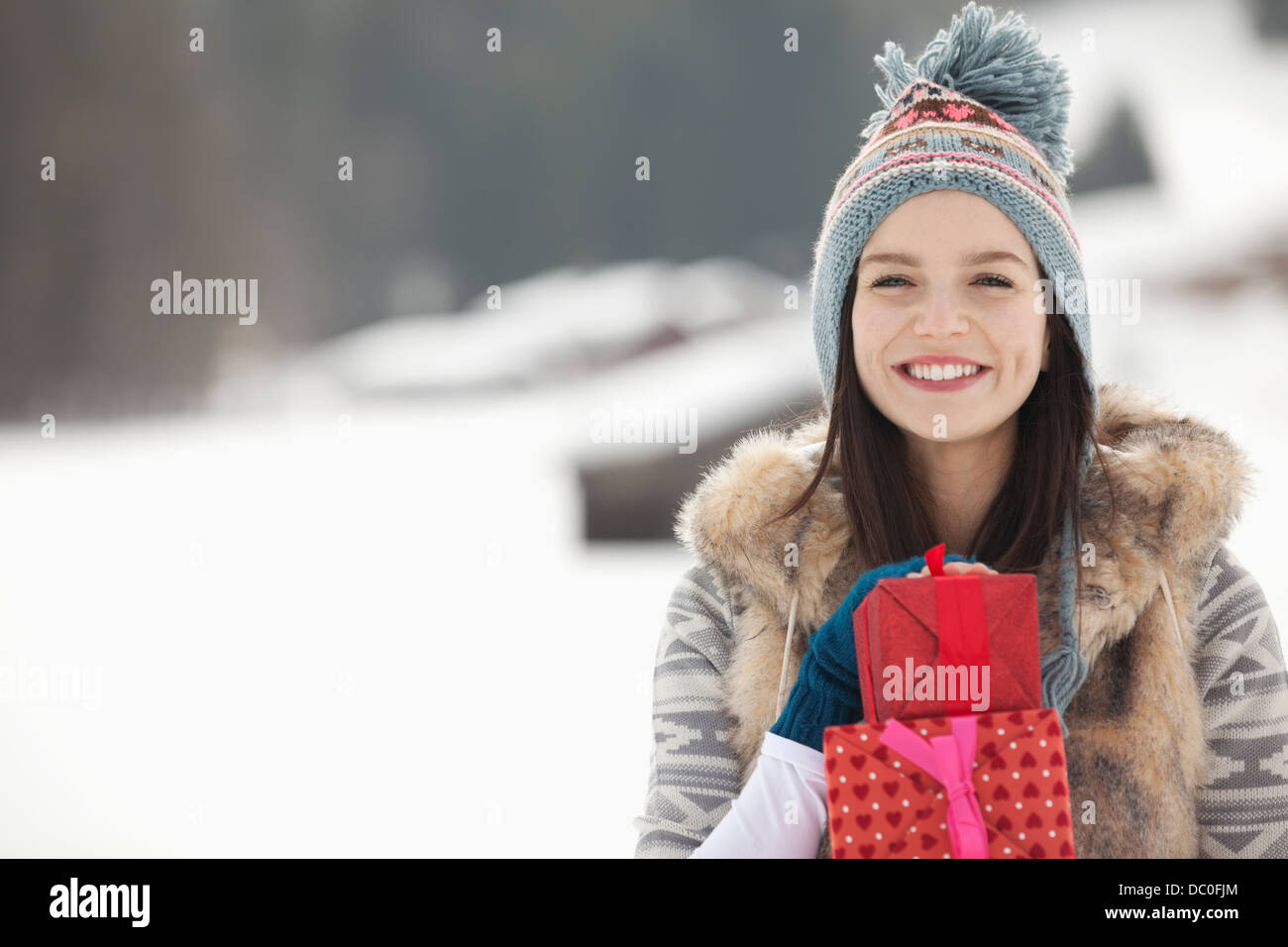 Porträt der lächelnde Frau mit Weihnachtsgeschenken in schneebedecktes Feld Stockfoto