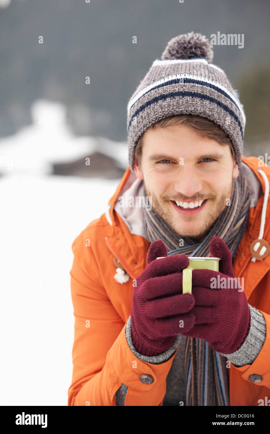 Porträt von lächelnden Mann in Strick Mütze und Handschuhe Kaffeetrinken in schneebedeckten Feld hautnah Stockfoto