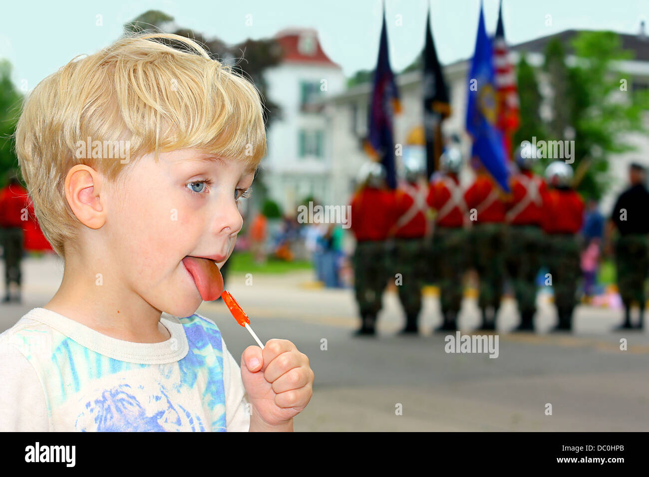 Ein Kind ist bei einer Parade. marschieren Sie ein Süßigkeiten-Liebhaber lecken, als militärische Mitglieder halten amerikanische Flaggen durch Stockfoto