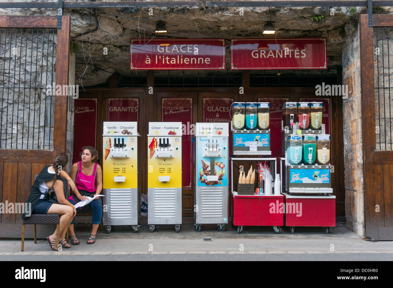 Zwei junge Frauen sitzen warten auf Touristen Speiseeis zu verkaufen, an einem heissen Sommertag in Brantôme, in der Dordogne im Südwesten Frankreichs, Europa. Stockfoto