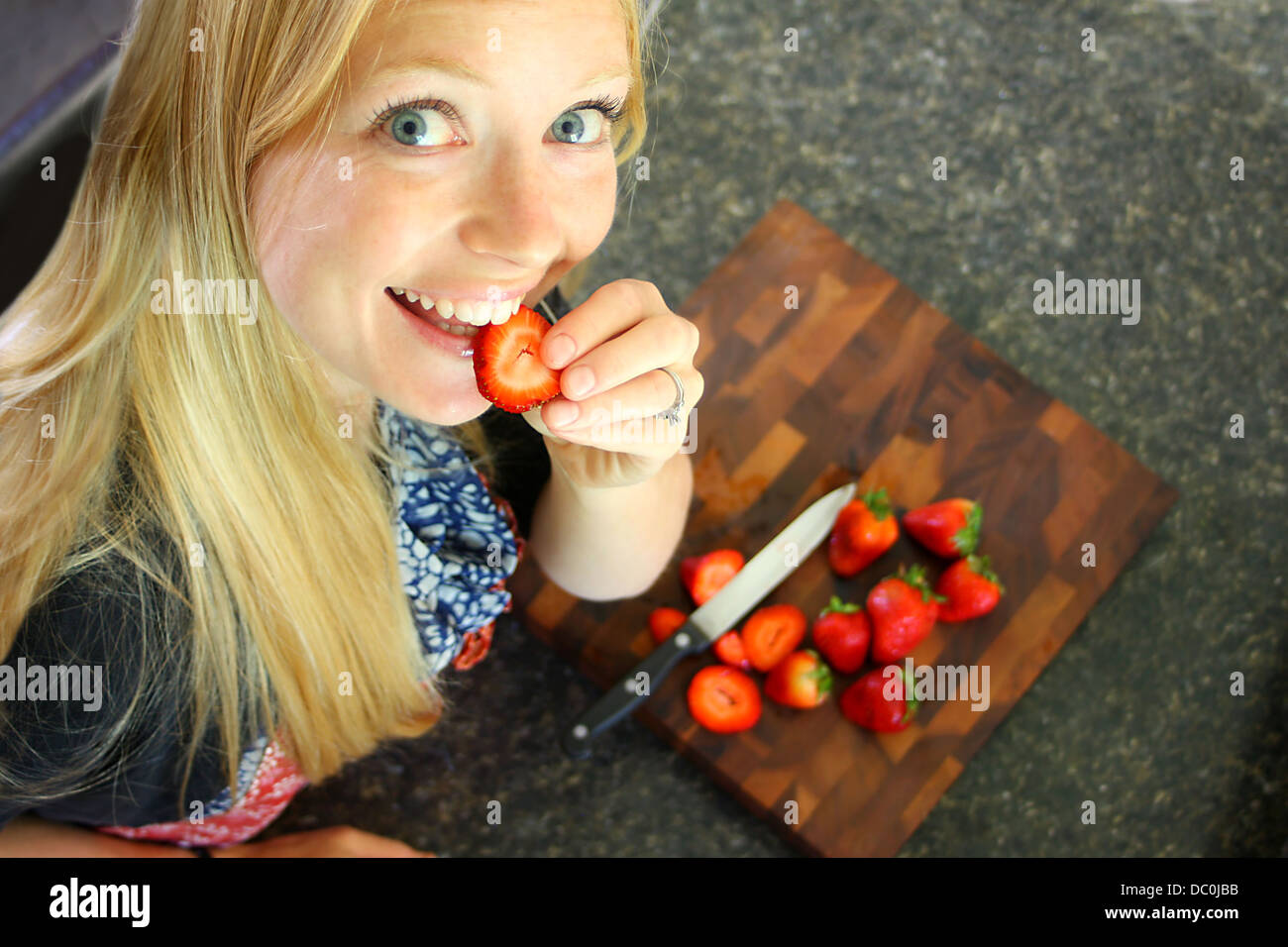 Eine attraktive Frau, die Verkostung einer Erdbeere während des Schneidens, gesundes Obst Stockfoto