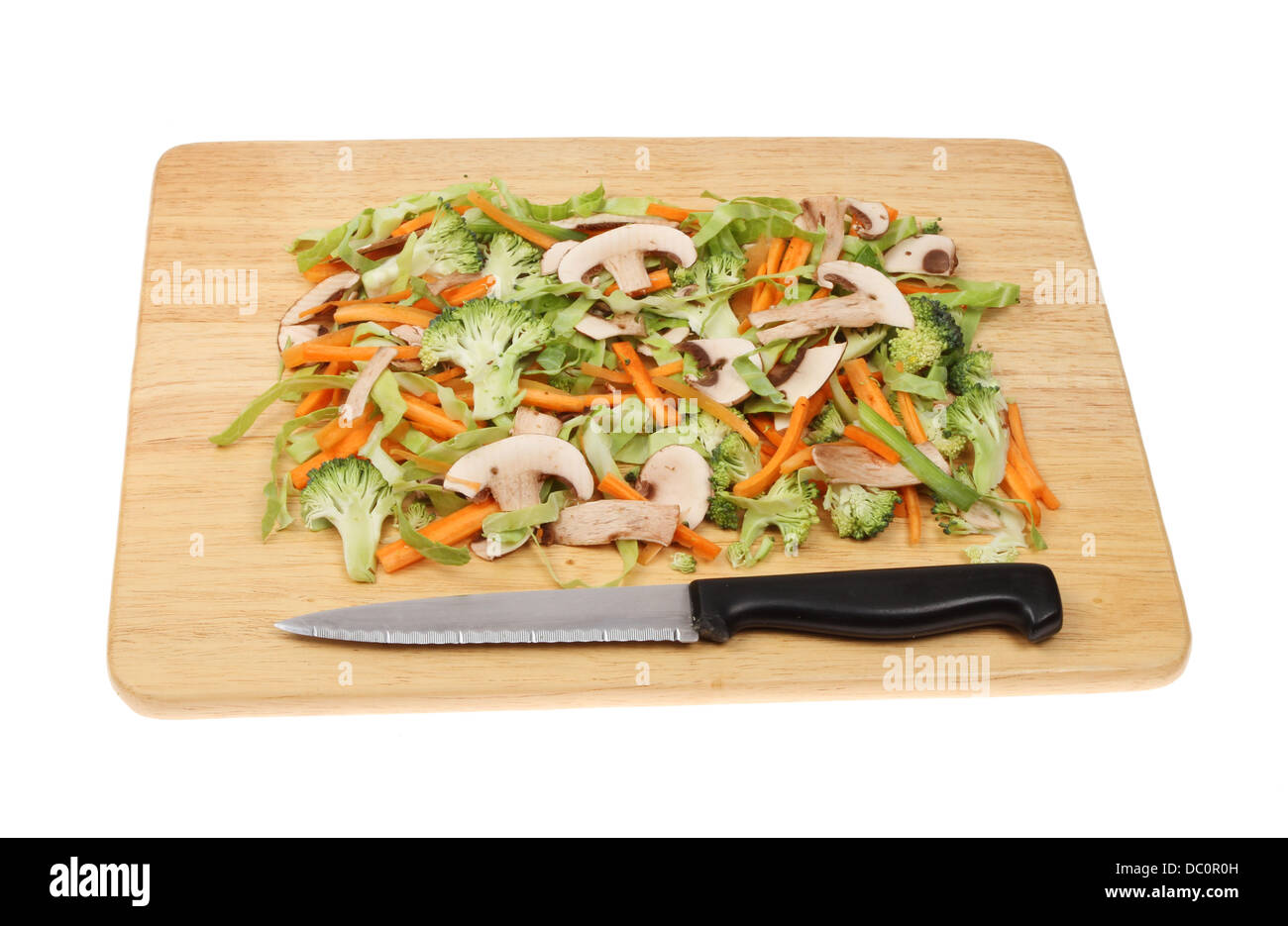Gehacktes Gemüse auf einem Holzbrett mit einem Messer isoliert gegen weiß Stockfoto