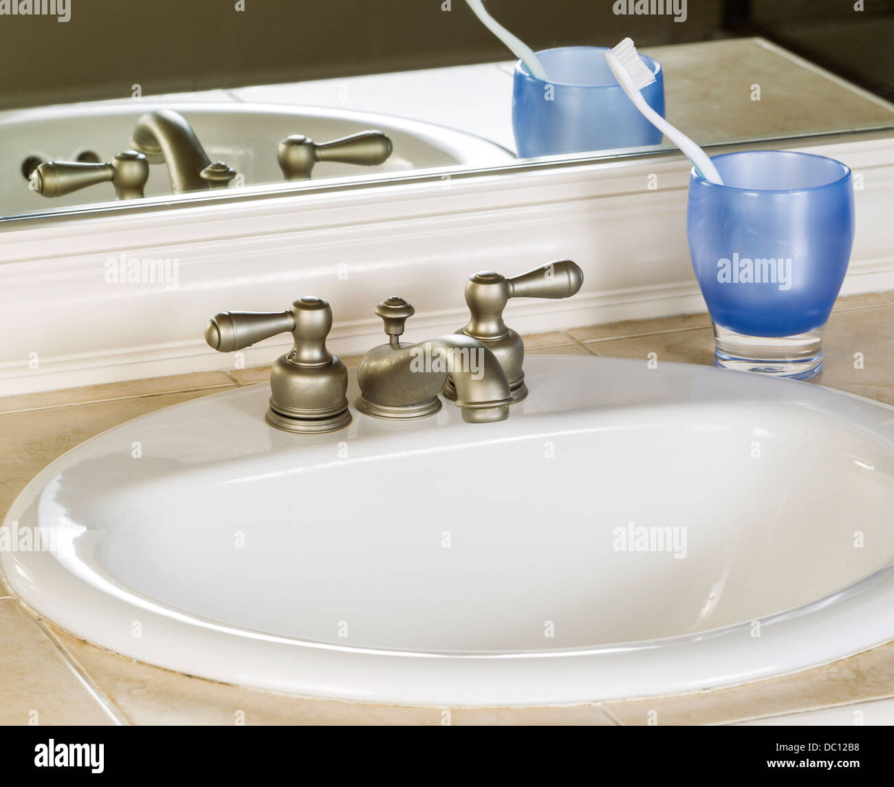 Foto von Waschbecken und Wasserhahn mit blauen Tasse, Zahnbürste und Spiegel im Hintergrund Stockfoto