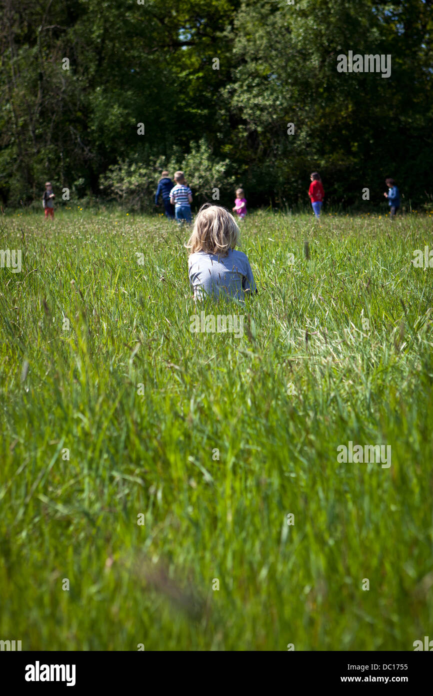 Junge sitzt im Feld weit weg von Freunden Stockfoto