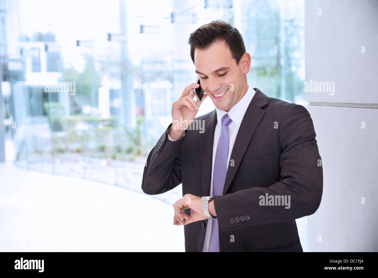 Geschäftsmann, reden über Handy und Armbanduhr schaute lächelnd Stockfoto