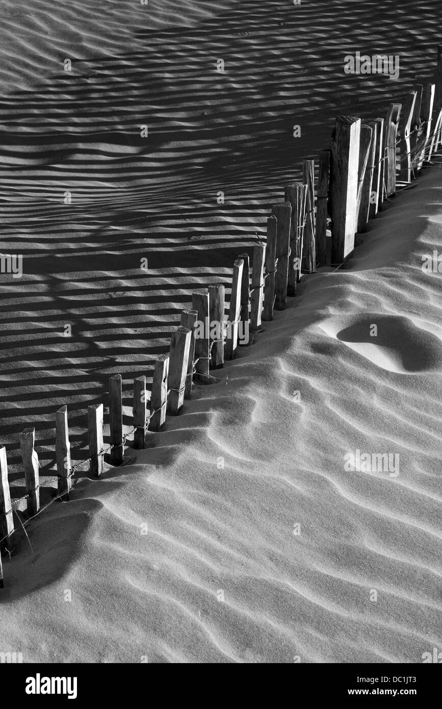 Holzzaun in Sanddünen mit starken Schatten aus Sonnenlicht Stockfoto