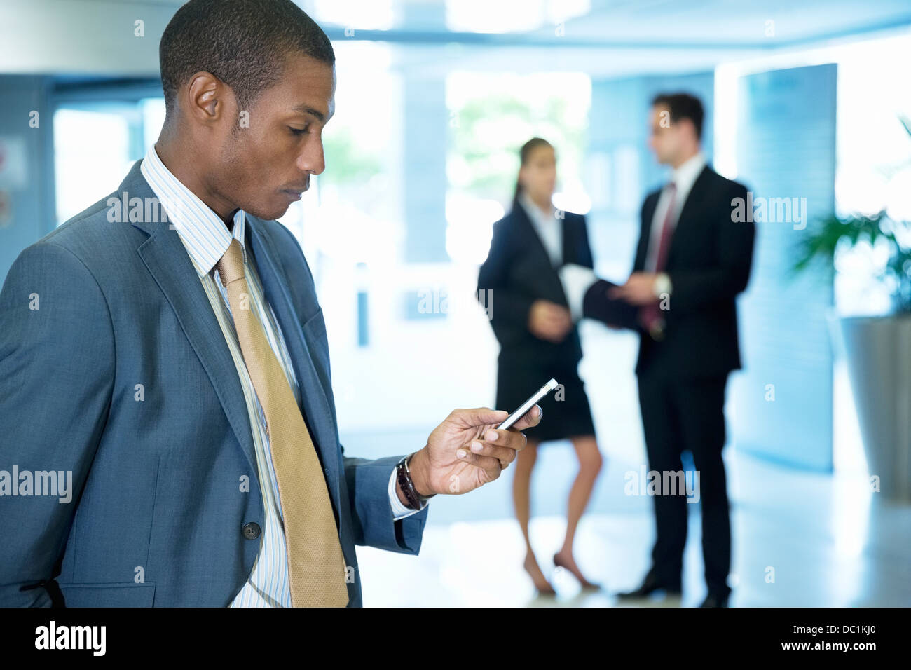 Geschäftsmann Text messaging mit Handy in lobby Stockfoto