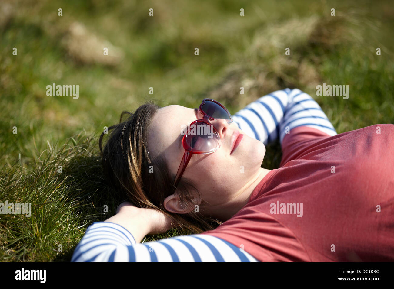 Junge Frau mit Herz Form Sonnenbrille liegen auf dem Rasen Stockfoto