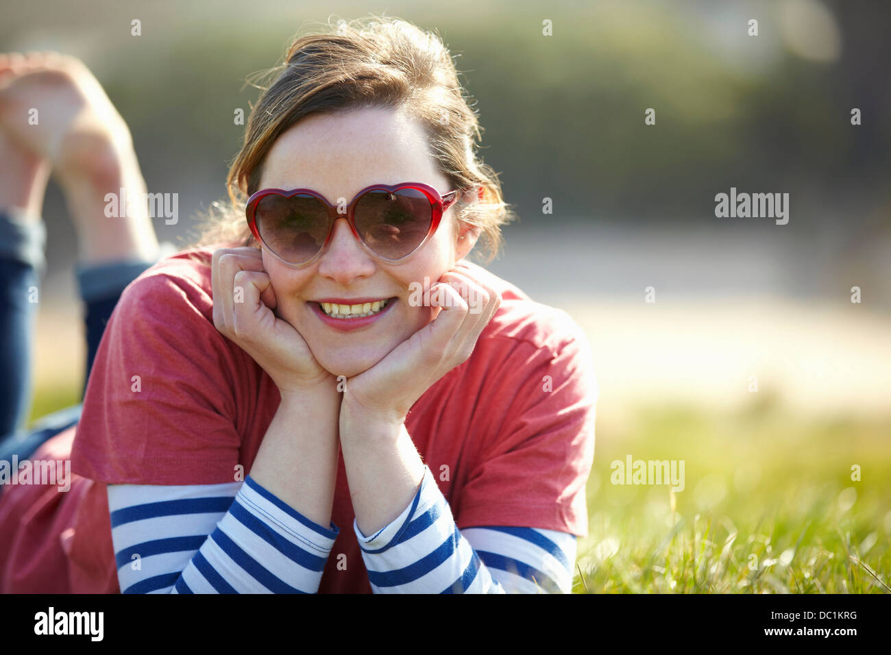 Porträt der jungen Frau mit Herz Form Sonnenbrille liegen auf dem Rasen Stockfoto