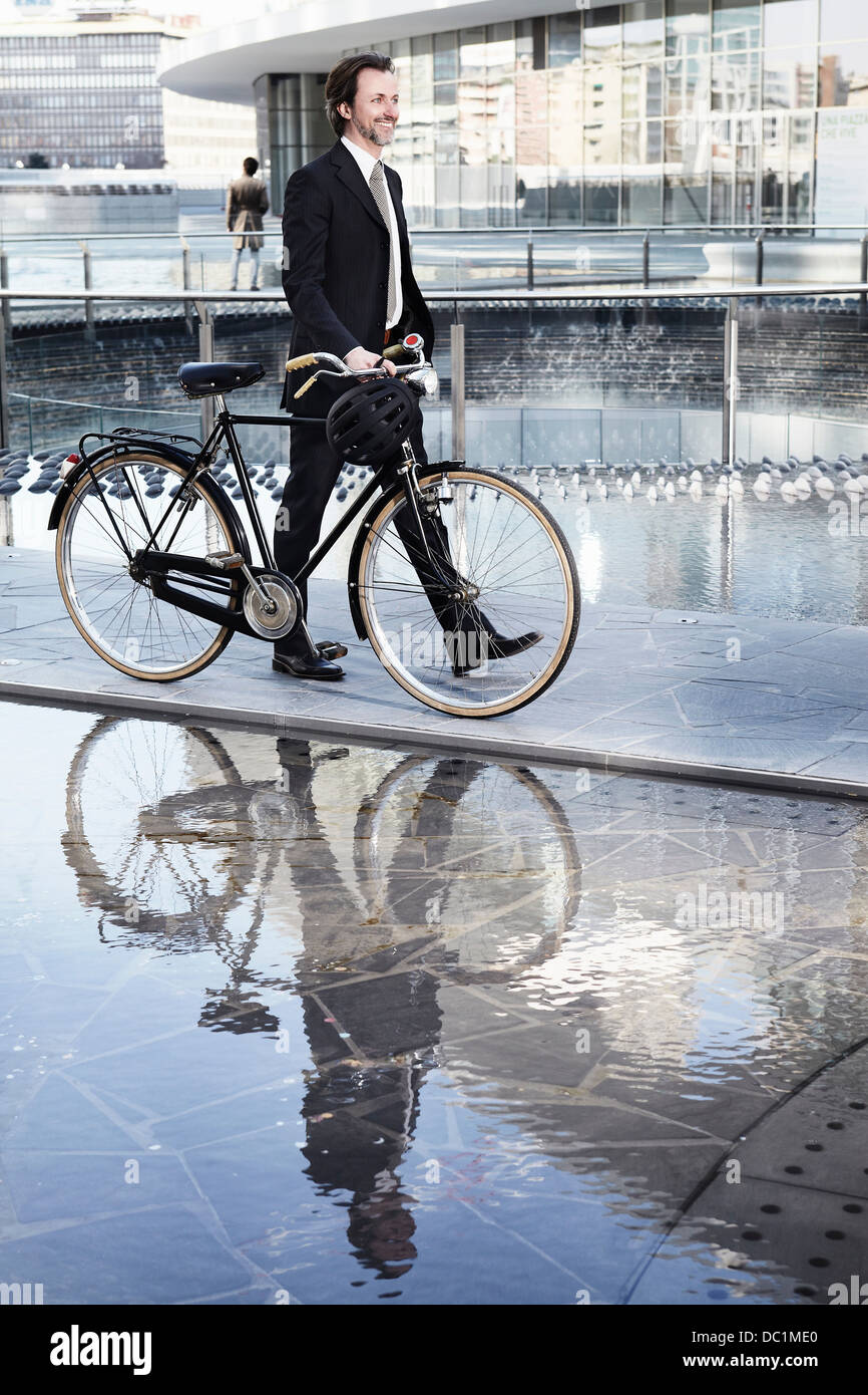 Mitte adult Geschäftsmann zu Fuß mit dem Fahrrad durch Wasserspiel in Stadt Stockfoto