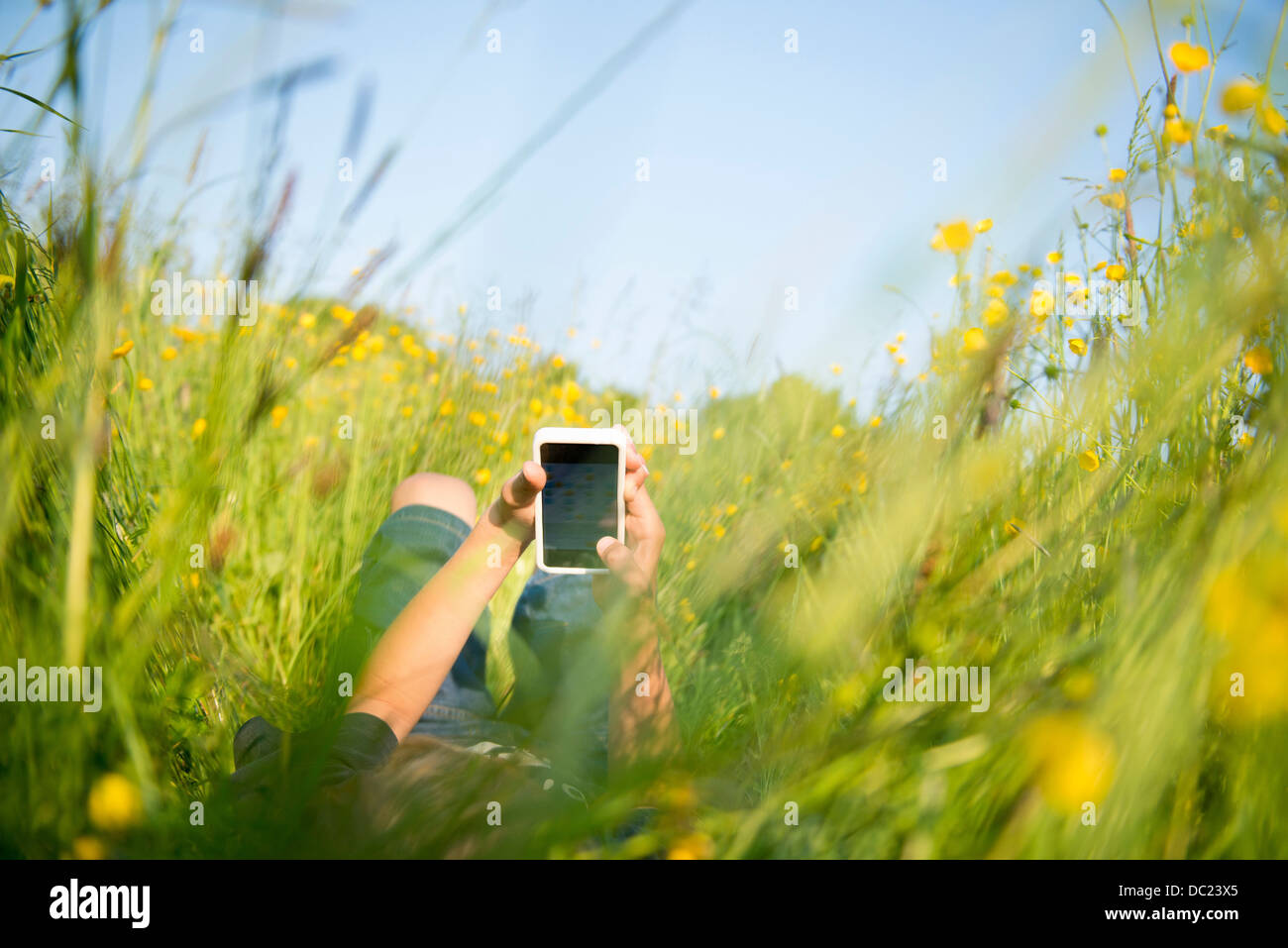 Junge liegend lange Gras auf Smartphone spielen Stockfoto