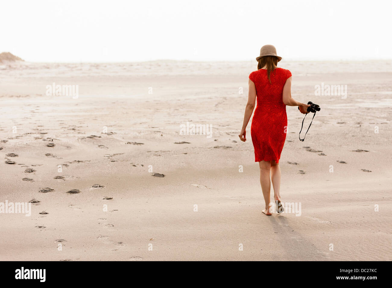 Reife Frau im roten Kleid zu Fuß am Strand Stockfoto