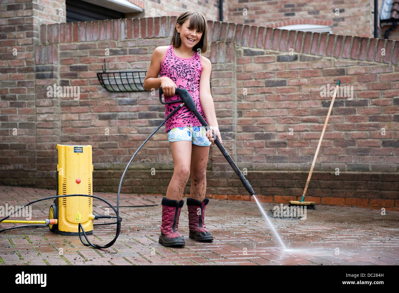 Eine Mädchen im Alter von 10 verwendet einen Hochdruckreiniger zur Reinigung des Block ebnen Antrieb auf ihre Familie zu Hause für Taschengeld. Stockfoto