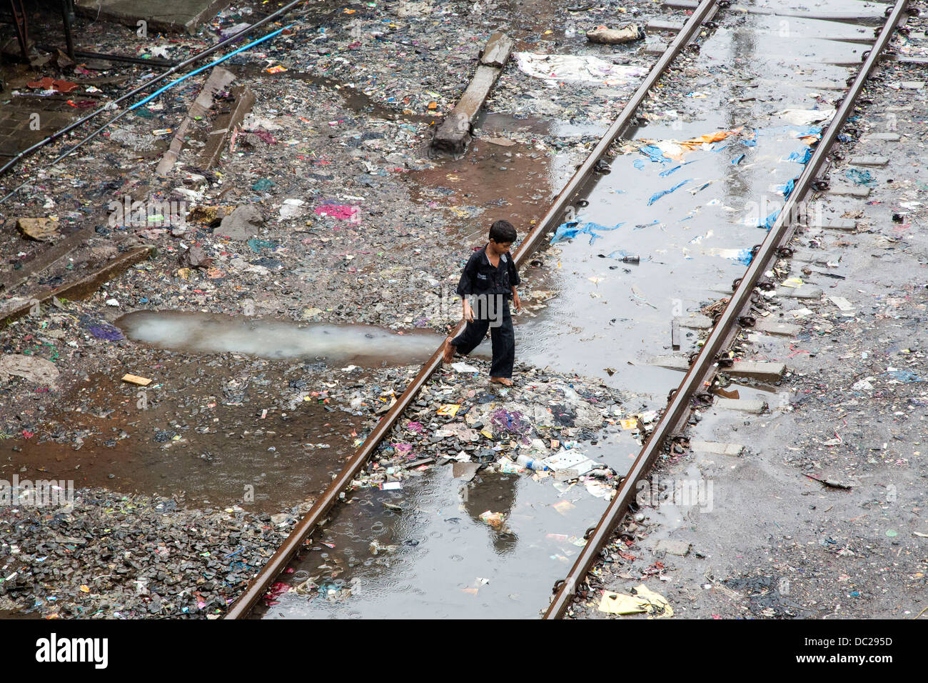 Junge geht durch Pfützen und Schmutz der Bandra Slumgebiet mit Schienen durch Stockfoto