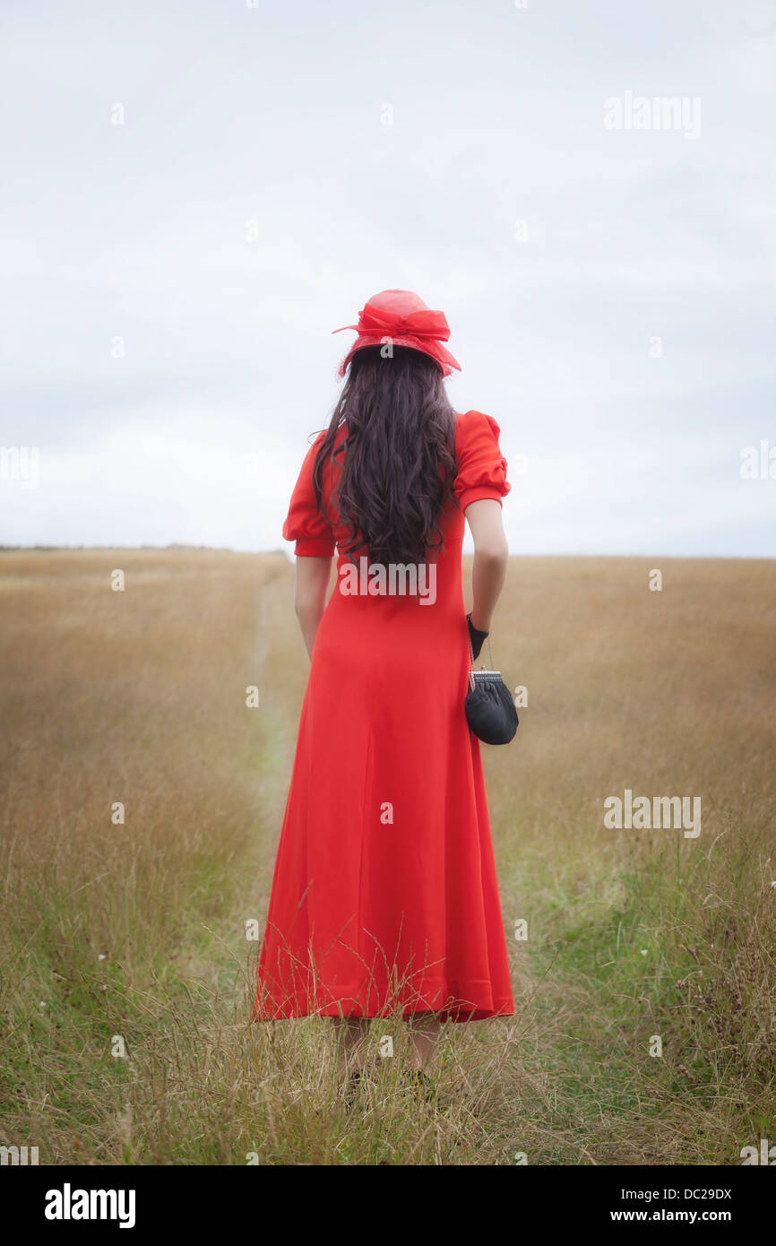 eine Frau in einem roten Kleid ist über ein Feld gehen. Stockfoto