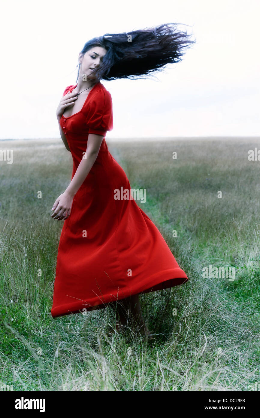 eine Frau in einem roten Kleid tanzt auf einem Feld Stockfoto
