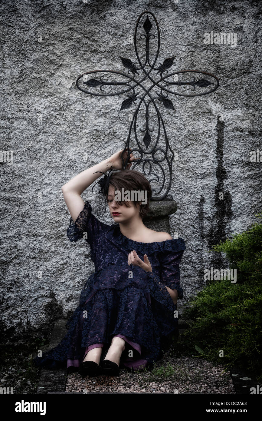 eine trauernde Frau mit Schleier und dunkles Kleid sitzt auf einem Grab Stockfoto