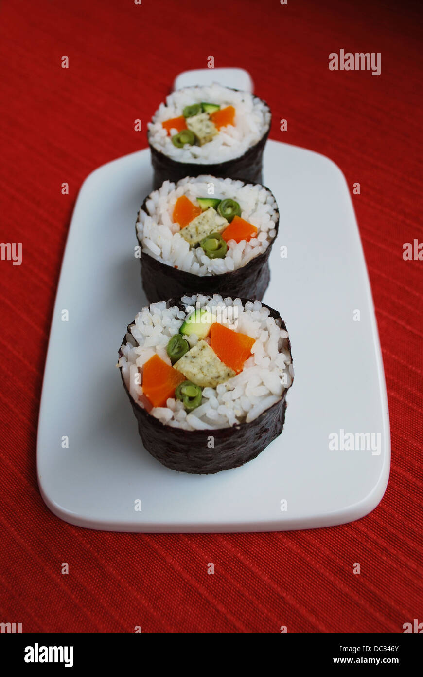 Vegetarische Maki Sushi-Rollen mit Reis, Karotten, Zucchini, grüne Bohnen, Tofu und Nori Algen in weiße Schale auf rotem Grund Stockfoto