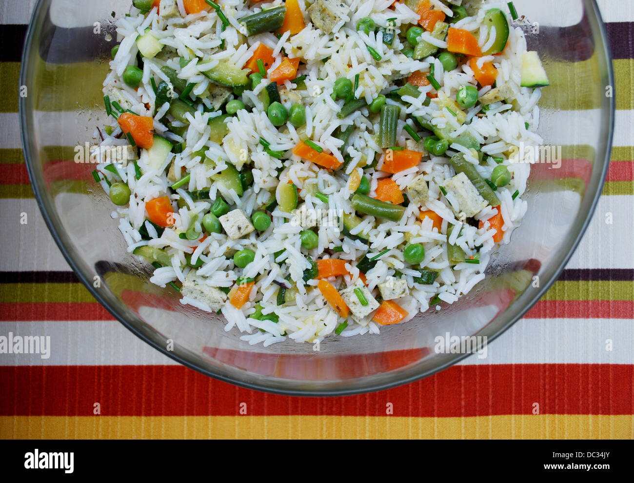 Vegetarischer Salat von weißem Reis mit gemischtem Gemüse und Tofu in eine Glasschüssel auf farbigen Hintergrund Stockfoto