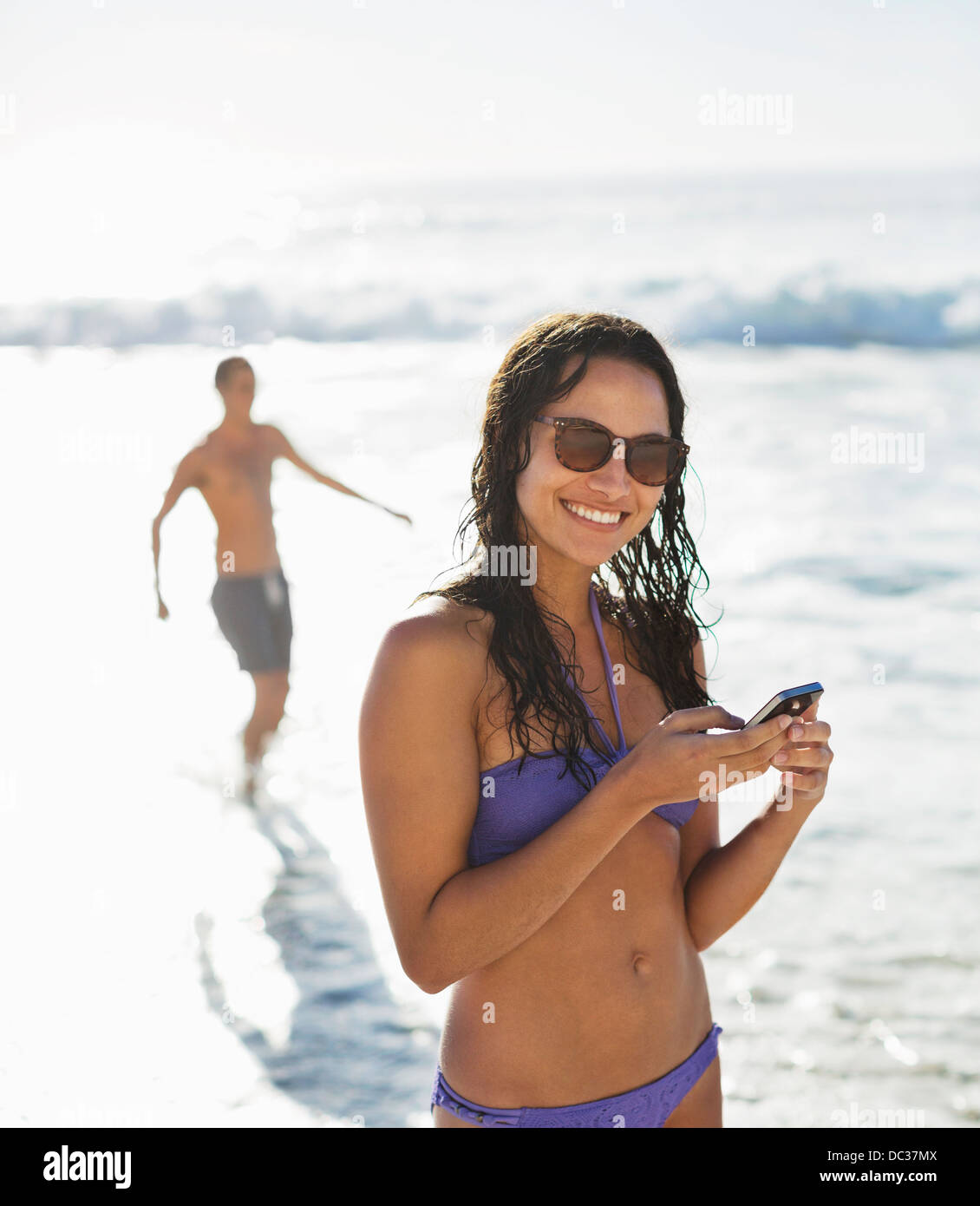 Porträt der lächelnde Frau im Bikini mit Handy am Strand Stockfoto