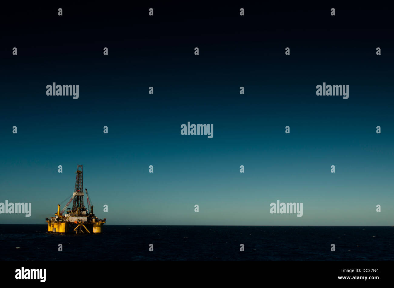 Offshore-Öl-Bohrinsel fern am Horizont, auf der linken Unterseite des Rahmens positioniert.  Blauer Himmel. Stockfoto
