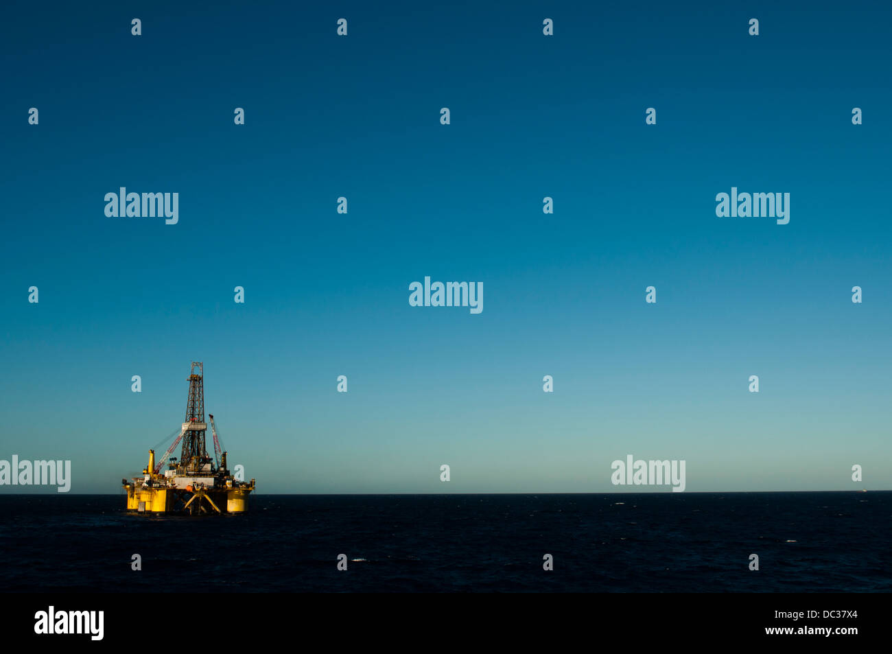 Offshore-Öl-Bohrinsel fern am Horizont, auf der linken Unterseite des Rahmens positioniert.  Blauer Himmel. Stockfoto