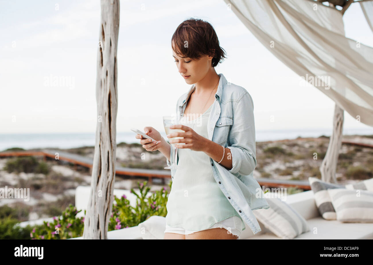 Frau trinkt Wein und Text-messaging mit Handy auf Terrasse Stockfoto