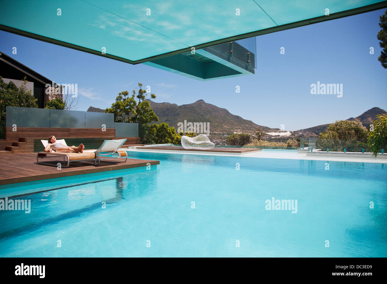 Frau Sonnenbaden auf Liegestuhl am Pool mit Blick auf die Berge Stockfoto