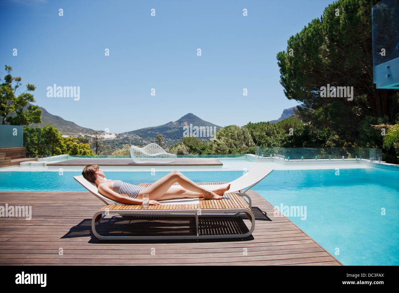 Frau Sonnenbaden auf Liegestuhl neben Luxus-Pool mit Blick auf die Berge Stockfoto