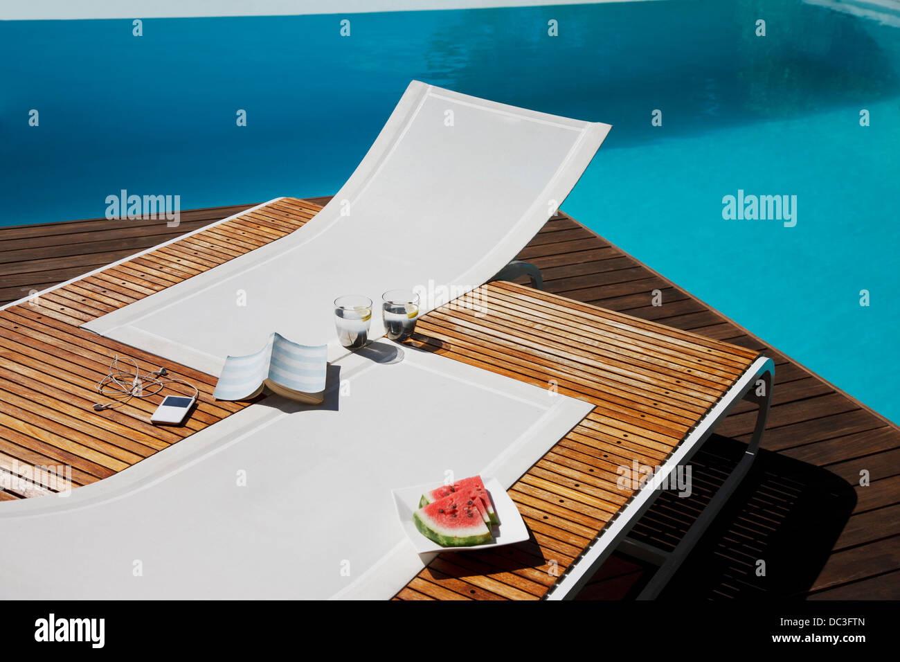Buch, MP3-Player, Wasser und Wassermelone auf den Liegestühlen am Pool Stockfoto