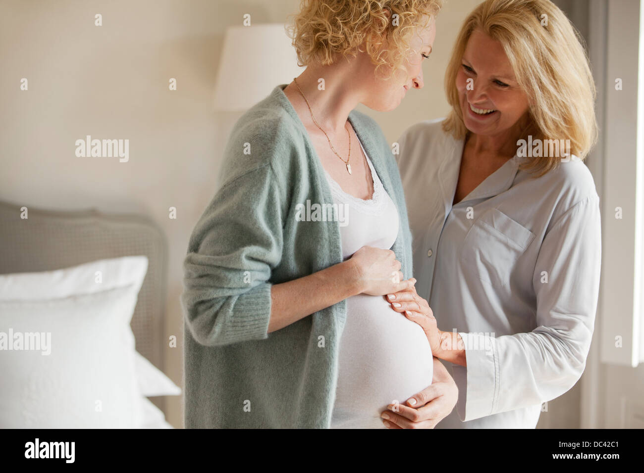 Lächelnde Mutter berühren schwangere Tochter Magen Stockfoto
