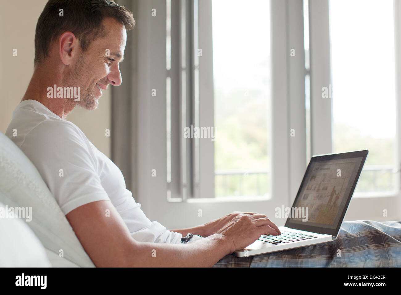 Lächelnder Mann mit Laptop im Bett Stockfoto