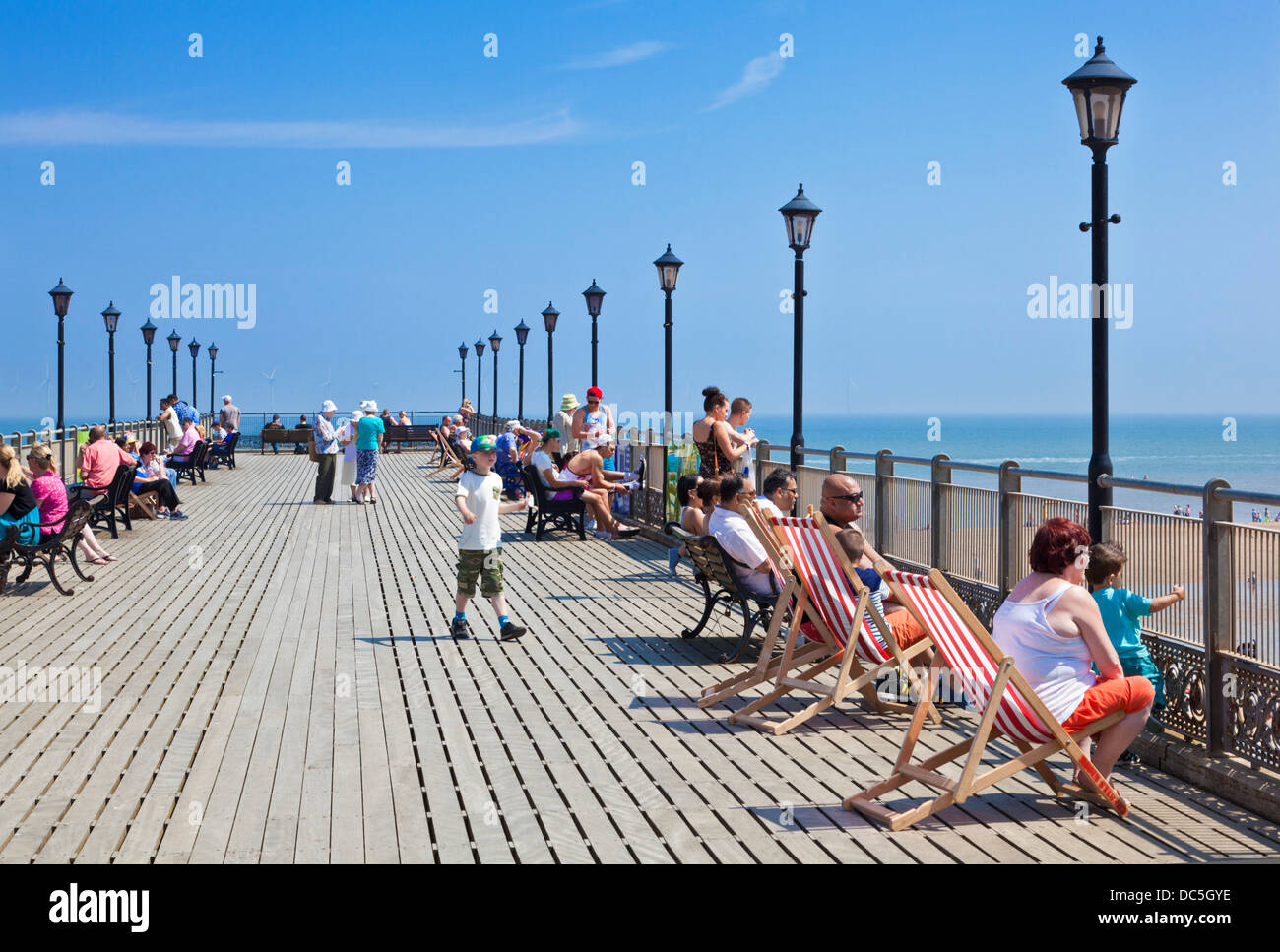 Leute sitzen auf Liegestühlen entlang der Seiten des Piers in Skegness Lincolnshire England UK GB EU Europa Stockfoto