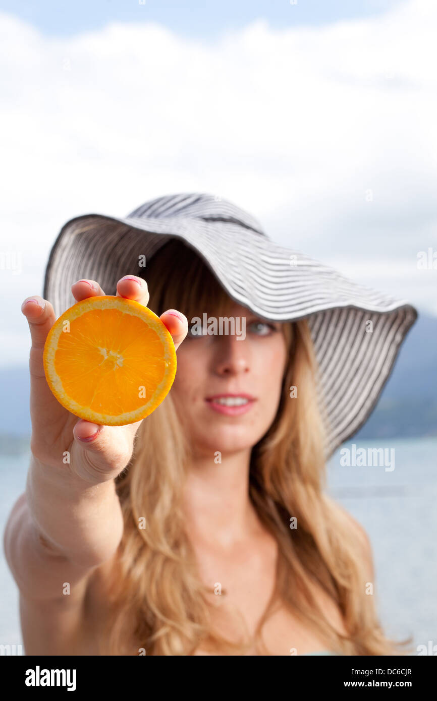 Eine blonde Kaukasische Frau hält eine Orangenscheibe. Stockfoto