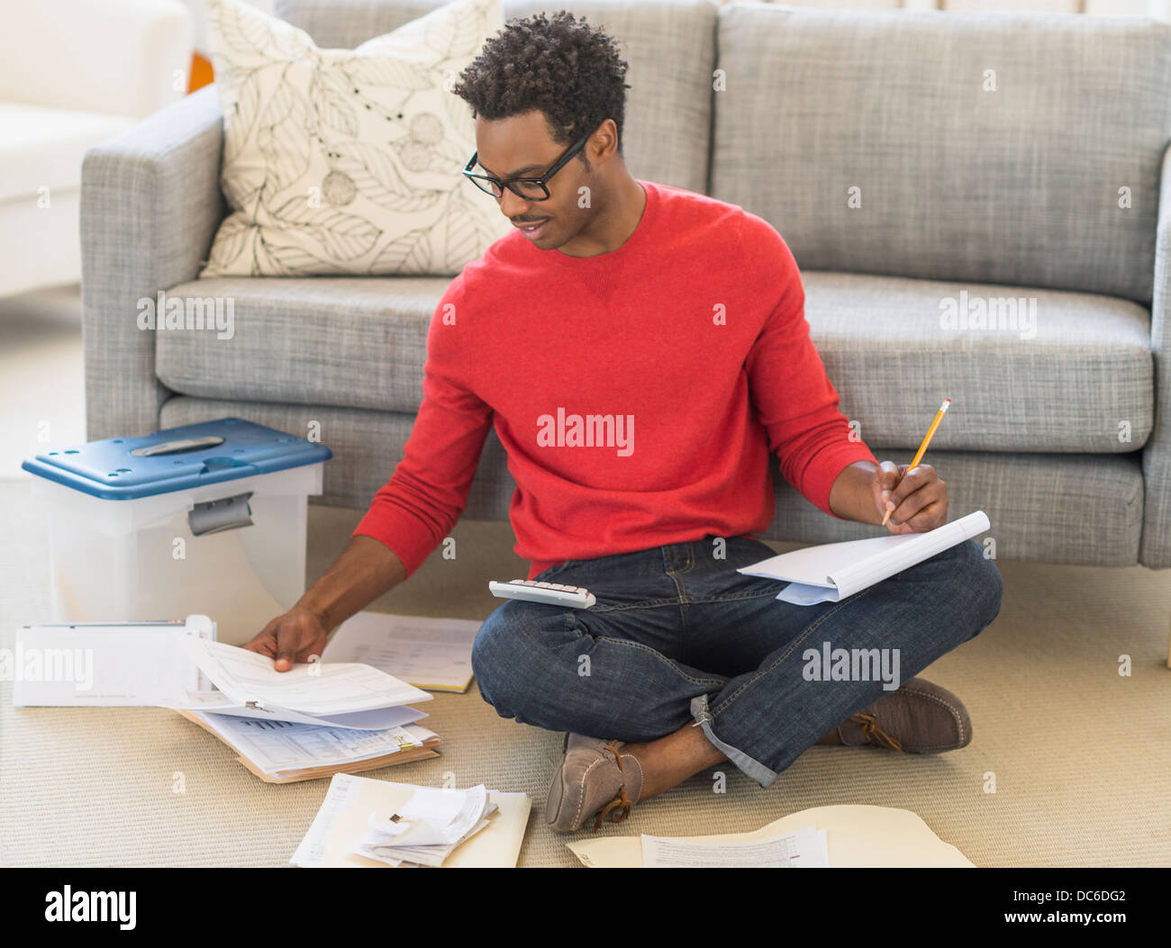 Mann sitzt auf dem Fußboden im Wohnzimmer und Berechnung Rechnungen Stockfoto