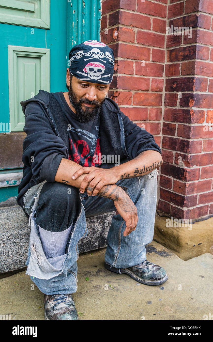 Bandenmitglied Hispanic sitzt auf einem vorderen Stoop eines Hauses in St. John, Nova Scotia mit tätowierten Armen und schwarzen Kopftuch. Stockfoto