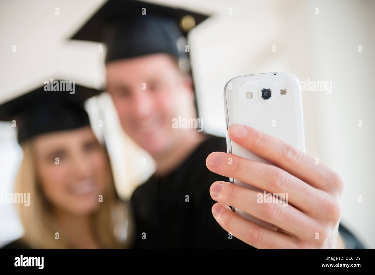Paar Freunde in Graduierung Kleider fotografieren mit smartphone Stockfoto