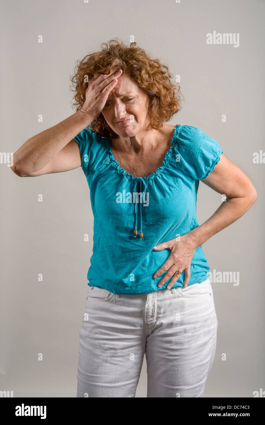 Eine 50 Jahre alte Auburn dunkelhaarige Frau zeigt Bauchschmerzen. Stockfoto