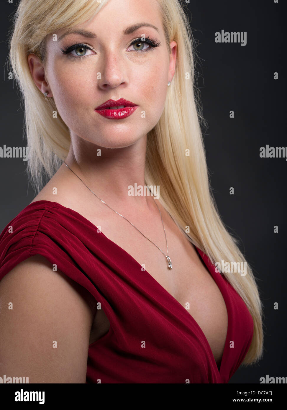 Schöne blonde kaukasischen Frau in ihren Zwanzigern tragen tief schneiden tief roten Kleid formelle Kleid Stockfoto