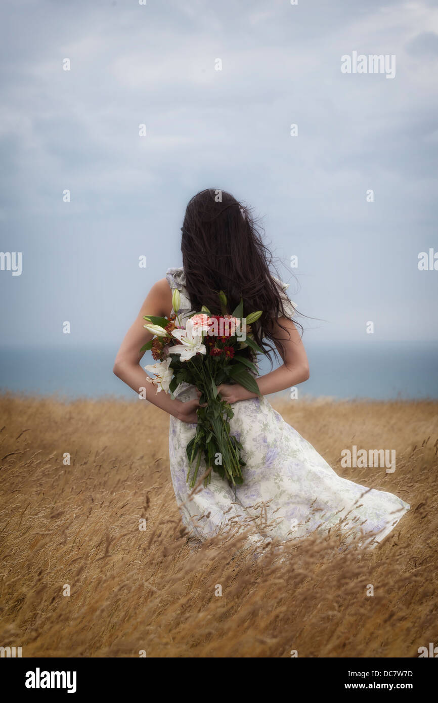 ein Mädchen in einem geblümten Kleid mit einem Strauß Blumen auf einem Feld Stockfoto