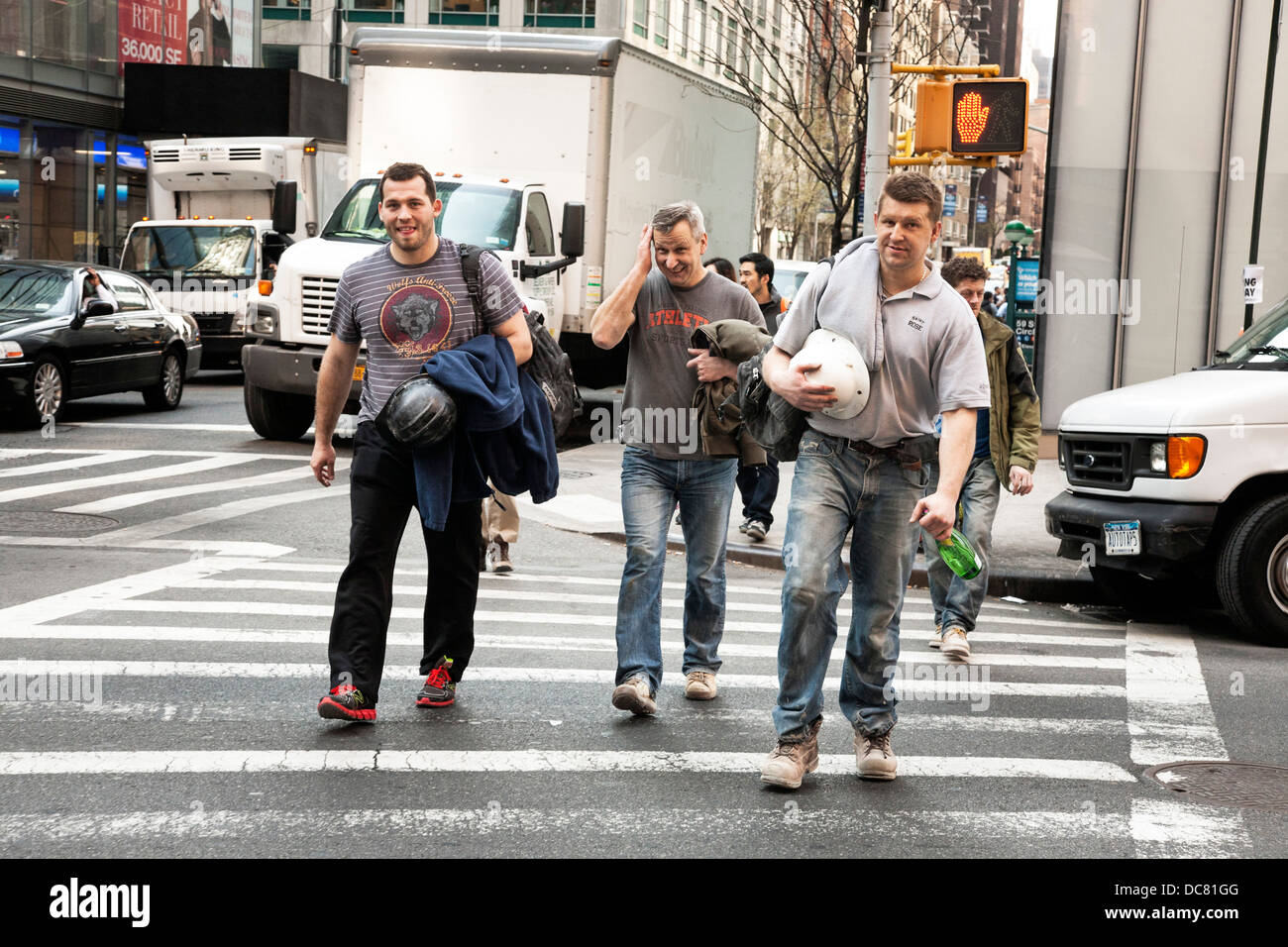 3 gut gelaunt Bauarbeiter in staubigen Stiefel Arbeit & tragen Schutzhelme überqueren Broadway nach der Arbeit in Midtown Manhattan Stockfoto