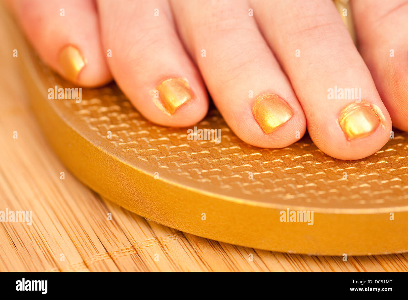 Frau stehend auf Bambusmatte mit golden lackierten Fußnägel mit goldenen Flip flops Stockfoto